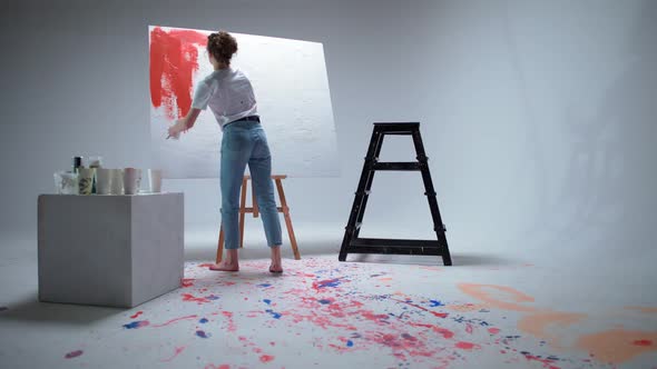 Female Artist Draws with a Brush on a Large Canvas in a White Room a Talented Artist Draws a Color
