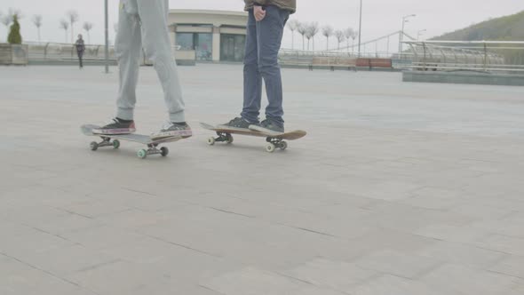 Legs of Teen Friends Skateboarding on City Square