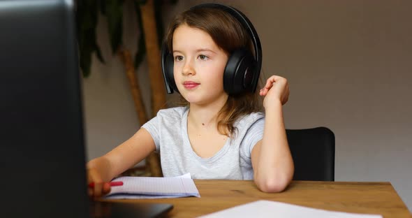 Cute little girl with headphones using laptop to study at home