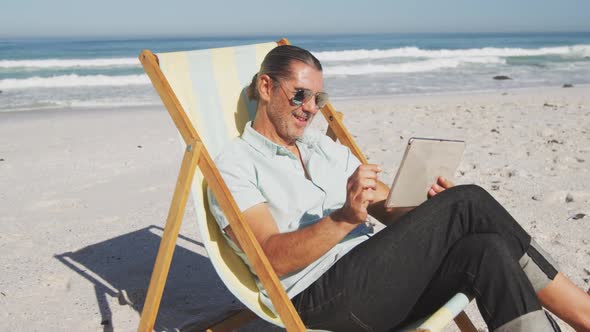 Senior Caucasian man sitting on sunbeds at the beach.