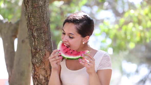 Beautiful young woman eating a slice of watermelon and smiling