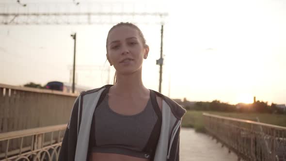 Young Caucasian Girl with Tied Blond Hair Taking Break After Running Along City Bridge at Sunset