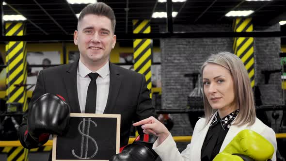 Man and a Woman Businessmen in Suits and Boxing Gloves Hold a Sign with a Dollar Sign in Their Hands