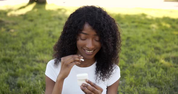 Young Black Woman Putting Wireless Earphones in Park