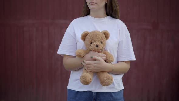 Unrecognizable Young Caucasian Woman Standing at Red Wall Outdoors Holding Teddy Bear