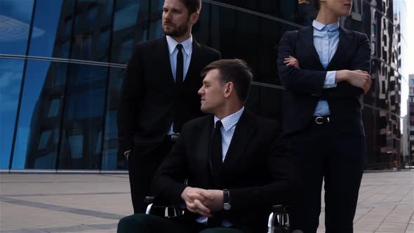 Epic Shot of Crippled Male with Disabled Legs Sitting on Wheelchair with His Colleagues