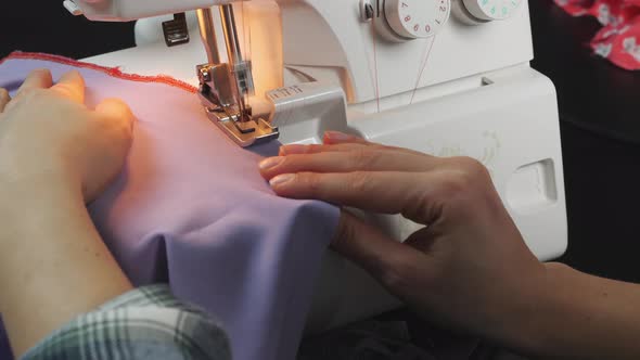 Female hands sew the edge of fabric on sewing machine.