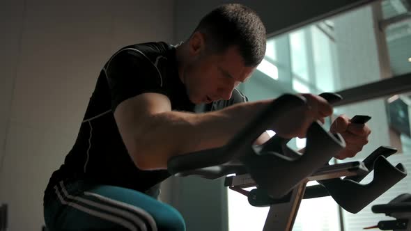 Caucasian Sportsman Swirling Pedals on a Stationary Bicycle in a Gym