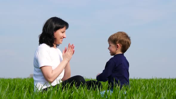 Happy Family: Mother and Child Sit on Green Grass and Play, Slapping Each Other on Batty