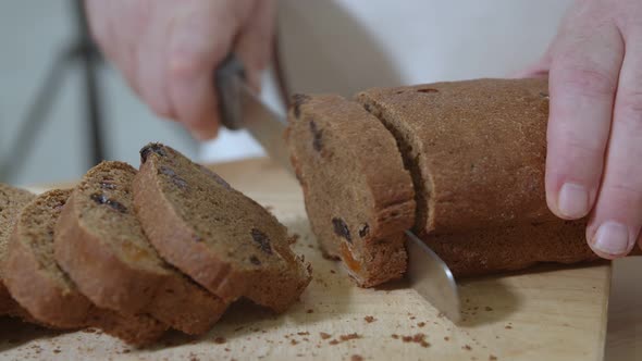 Baker is Cutting Baked Dutch Bread with Raisins and Dried Apricots with Knife