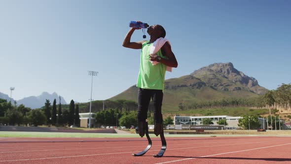 Disabled mixed race man with prosthetic legs standing on a race track and drinking water