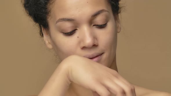 Beauty Portrait of Young African American Woman Twisting Off a Jar of Cream and Enjoying Its Aroma