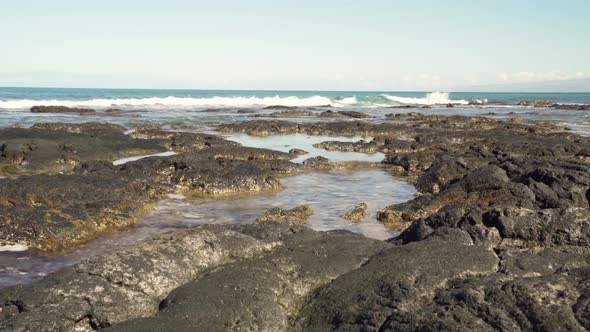 Small waves coming towards the camera covering a lava rock formation