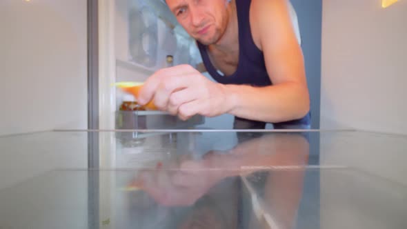 man looks into an empty refrigerator and takes out bottle of alcohol. Alcoholism