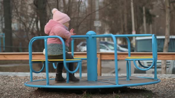 Lonely Little Kid Girl Spinning on a Carousel at Children's Playground