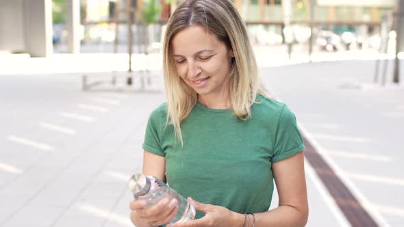 Blond woman holding in city showing bottle with clear water