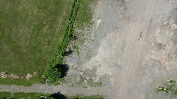 Green trees grass and plants contrast with grey construction gravel dirt, aerial