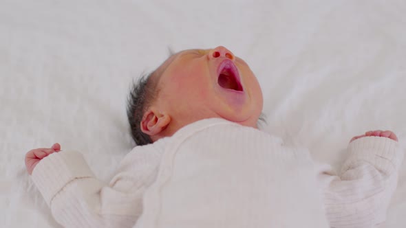 happy newborn baby lying sleeps and yawning on a white blanket