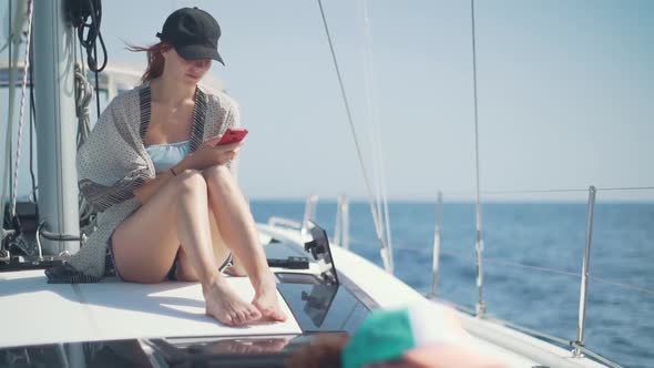 Beautiful Woman on a Yacht with Smartphone in Hands on the Background of the Islands of Ibiza or