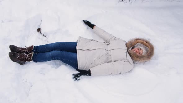 A Woman Lies in the Snow Raises Her Hands Up and Down As If Flapping Her Wings and Making an Angel