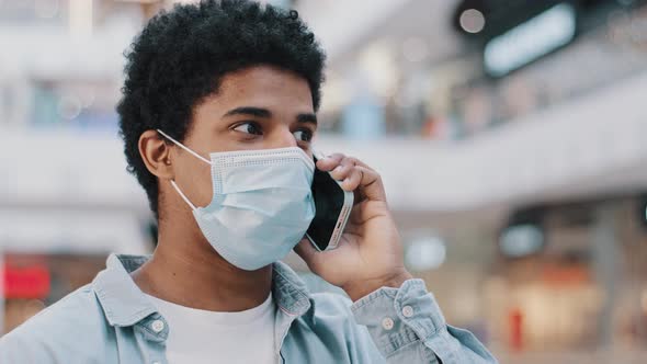 Closeup African American Guy in Medical Face Protective Mask Talking Mobile Phone Answering Call