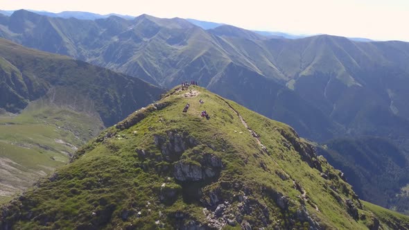 Hikers on hilltop high in mountains of Romania near Negoiu Peak. Aerial view from drone descending,