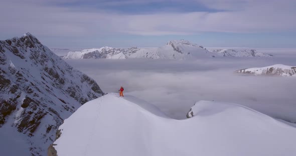 Aerial drone view of a mountain climber skier on the peak summit top of a snow covered mountain