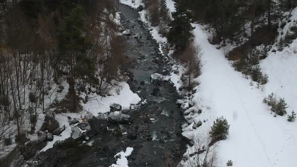 Aerial view of small river in rural countryside on snowing winter day, drone shot