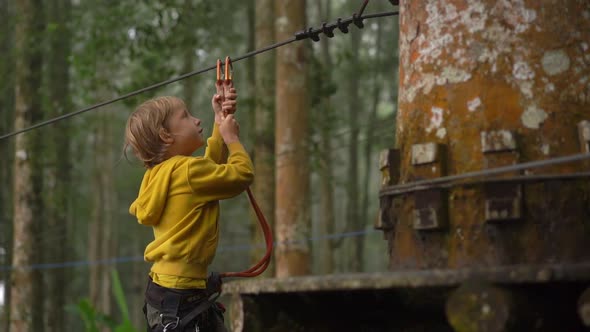 Superslowmotion Shot of a Little Boy in a Safety Harness Climbs on a Route in Treetops in a Forest