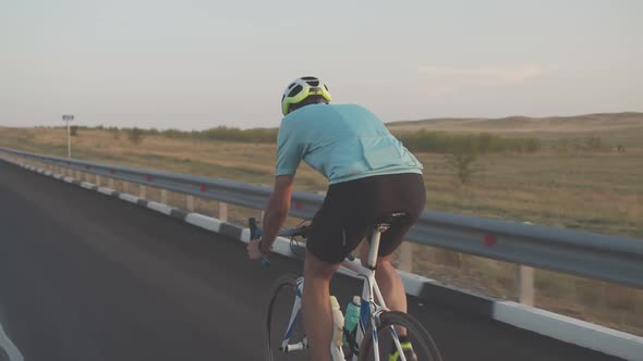 Back View of a Male Cyclist in Black Shorts, Blue T-shirt, Helmet and Sunglasses Riding a White Bike