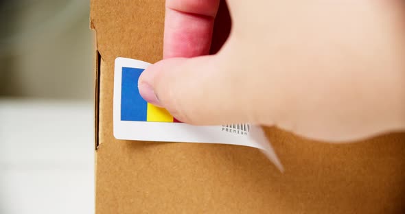 Hands applying MADE IN ROMANIA flag label on a shipping cardboard box with products. Close up shot w