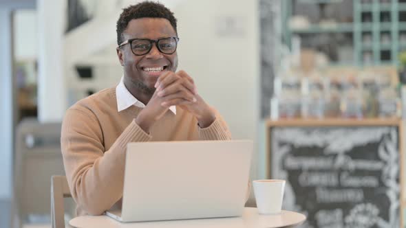 Creative African Man Smiling at Camera While Working on Laptop