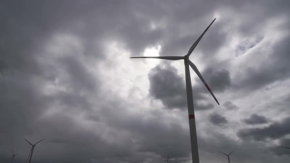 Motion the Blades of a Large Wind Turbine in a Field Against a Background of Cloudy Grey Sky on the