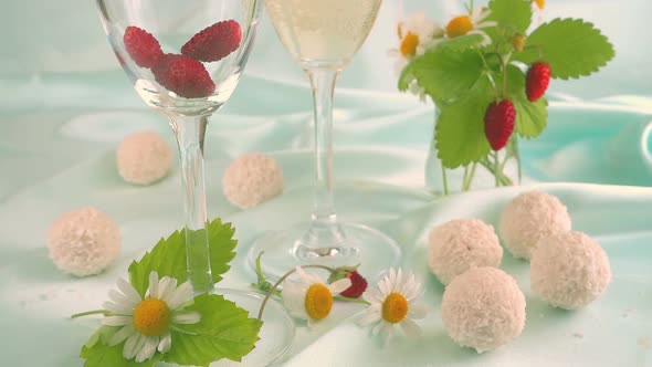 Glasses with sparkling wine, strawberries and round candy with coconut flakes on a blue background. 