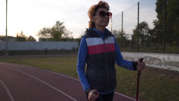 Senior Woman Training with Walking Poles at Stadium