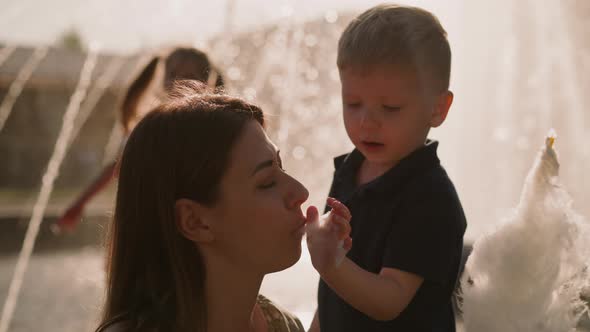 Little Boy Feeds Mother with Spun Sugar Against Fountain