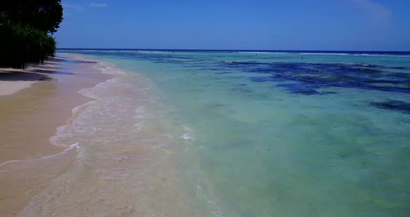 Wide angle aerial clean view of a sandy white paradise beach and blue sea background in vibrant 4K