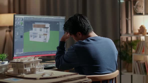 Asian Male Engineer Having A Headache While Designing House On A Desktop At Home