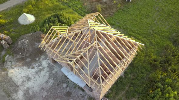 Aerial view of unfinished brick house with wooden roof structure under construction.