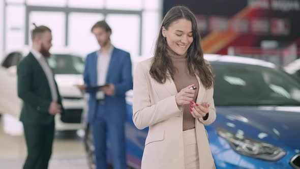 Happy Young Beautiful Caucasian Woman Admiring Car Keys As Men Talking at Background