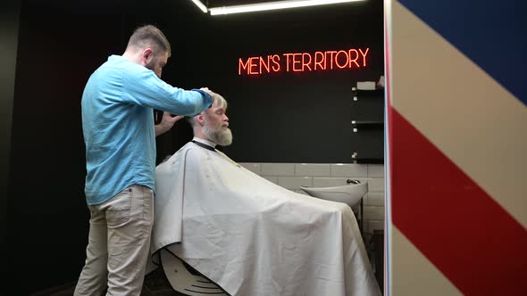 Barber work in a salon for men. A gray-haired man gets a haircut