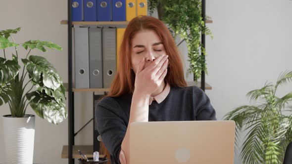 bored red hair female student yawning near laptop in office