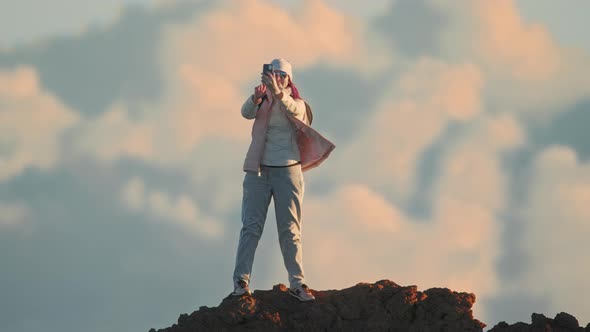 Happy Woman Using Smartphone Online on Top of Mountain Sunset Clouds Background