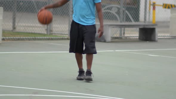Young man basketball player dribbling a basketball on an outdoor court.