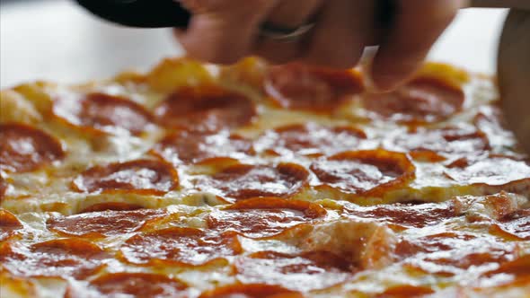 Woman's Hand Slicing the Salami Pizza Into Slices Using a Roller Pizza Cutter