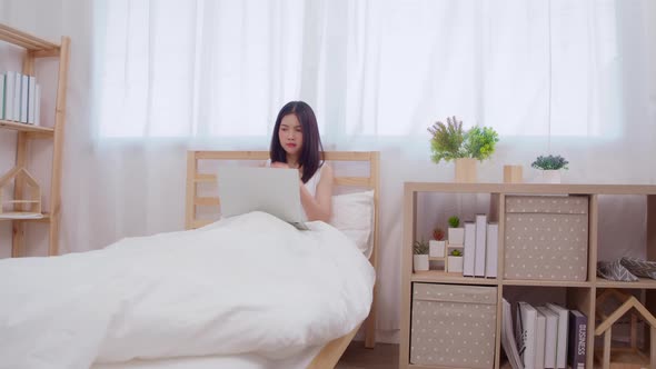 Young business freelance Asian woman working on laptop checking social media while lying on the bed.