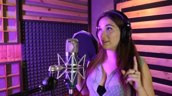 Woman with headphones dancing and singing in a studio on a retro microphone.