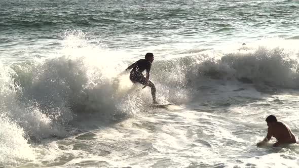 Skimboarding into a wave in slow motion at the beach during sunset in California