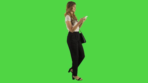 Texting while walking by a young businesswoman over a green screen. 4K