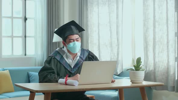 Asian Man Wearing Protection Face Mask And A Graduation Gown And Cap Having Video Call At Home